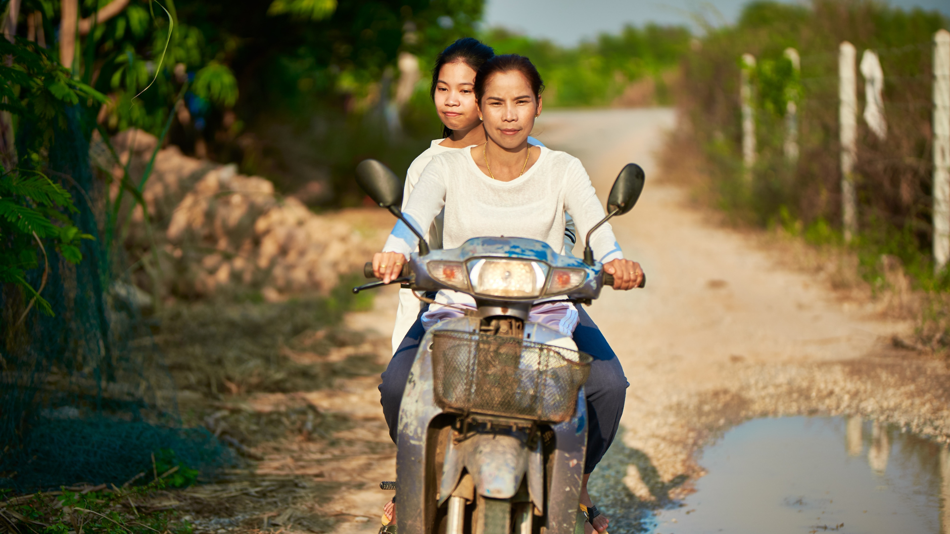 A mother and daughter riding a motorcycle on backroads in Asia.